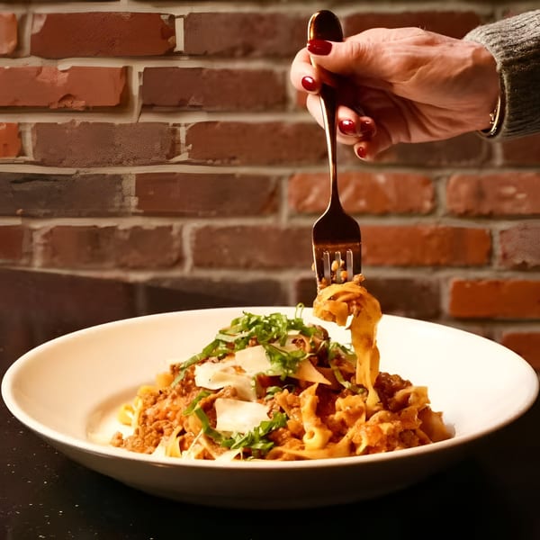 A hand with red nails twirls Ovest Via's tagliatelle bolognese with a fork against a brick wall.