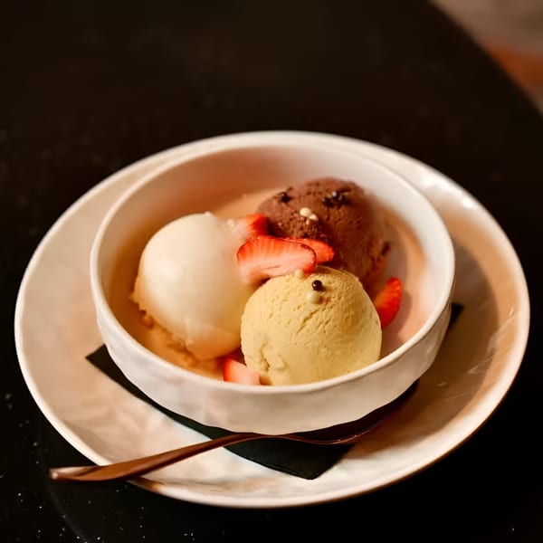 Three scoops of Ovest Via gelato with strawberries in a white bowl on a dark table.