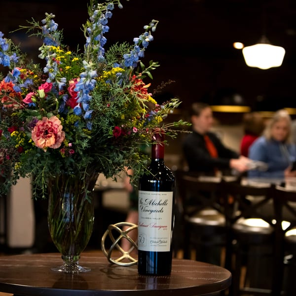A vibrant floral arrangement and a bottle of Chateau Ste. Michelle wine on a table in a restaurant.