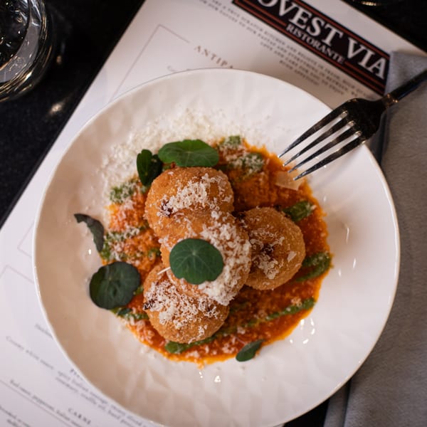 Italian arancini with tomato sauce, pesto, and grated cheese on a white plate with a fork.