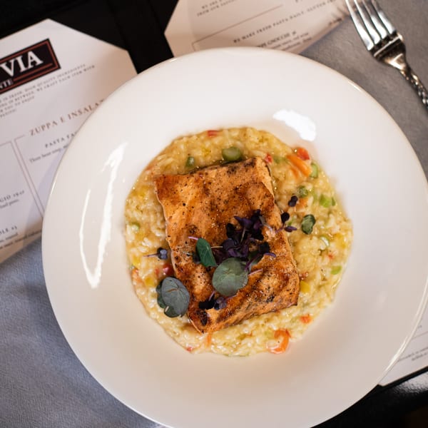 Ovest Via's grilled salmon with risotto, garnished with herbs, on a white plate.
