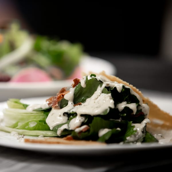 Close-up of a fresh salad with creamy dressing, bacon, and parmesan cheese on a white plate.