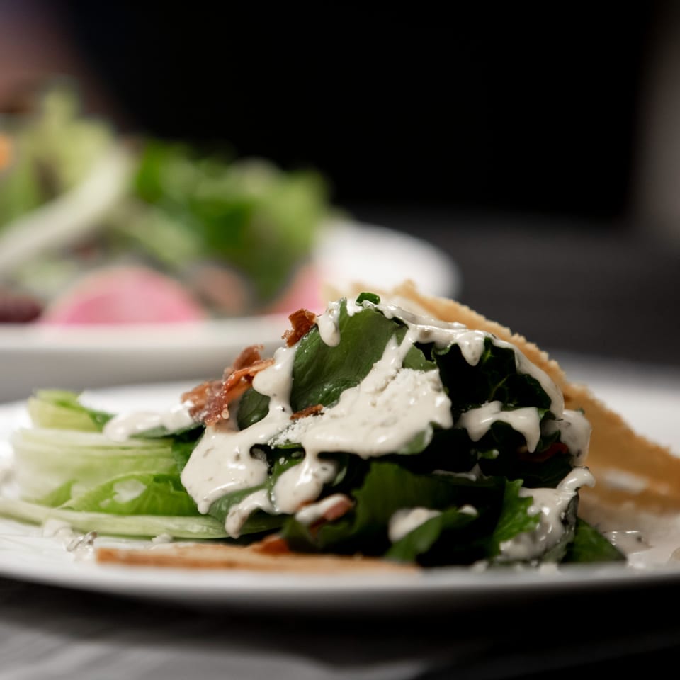 Close-up of a fresh salad with creamy dressing, bacon, and parmesan cheese on a white plate.